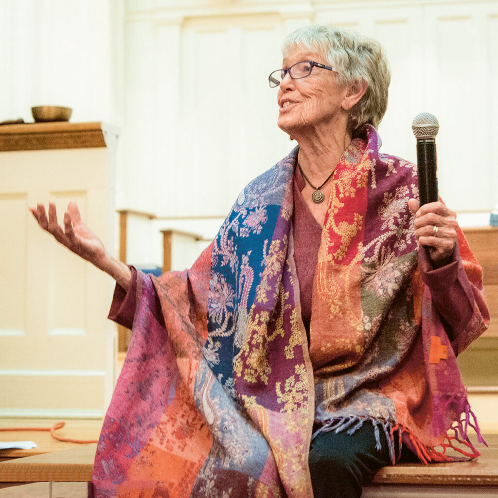 Joanna Macy in buten Umhang mit Mikrophon, freudig, erzählend, empfangend
