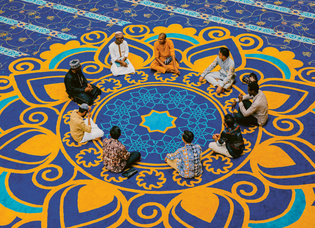 Männer, die im Kreis auf einem gemusterten Teppich sitzen.